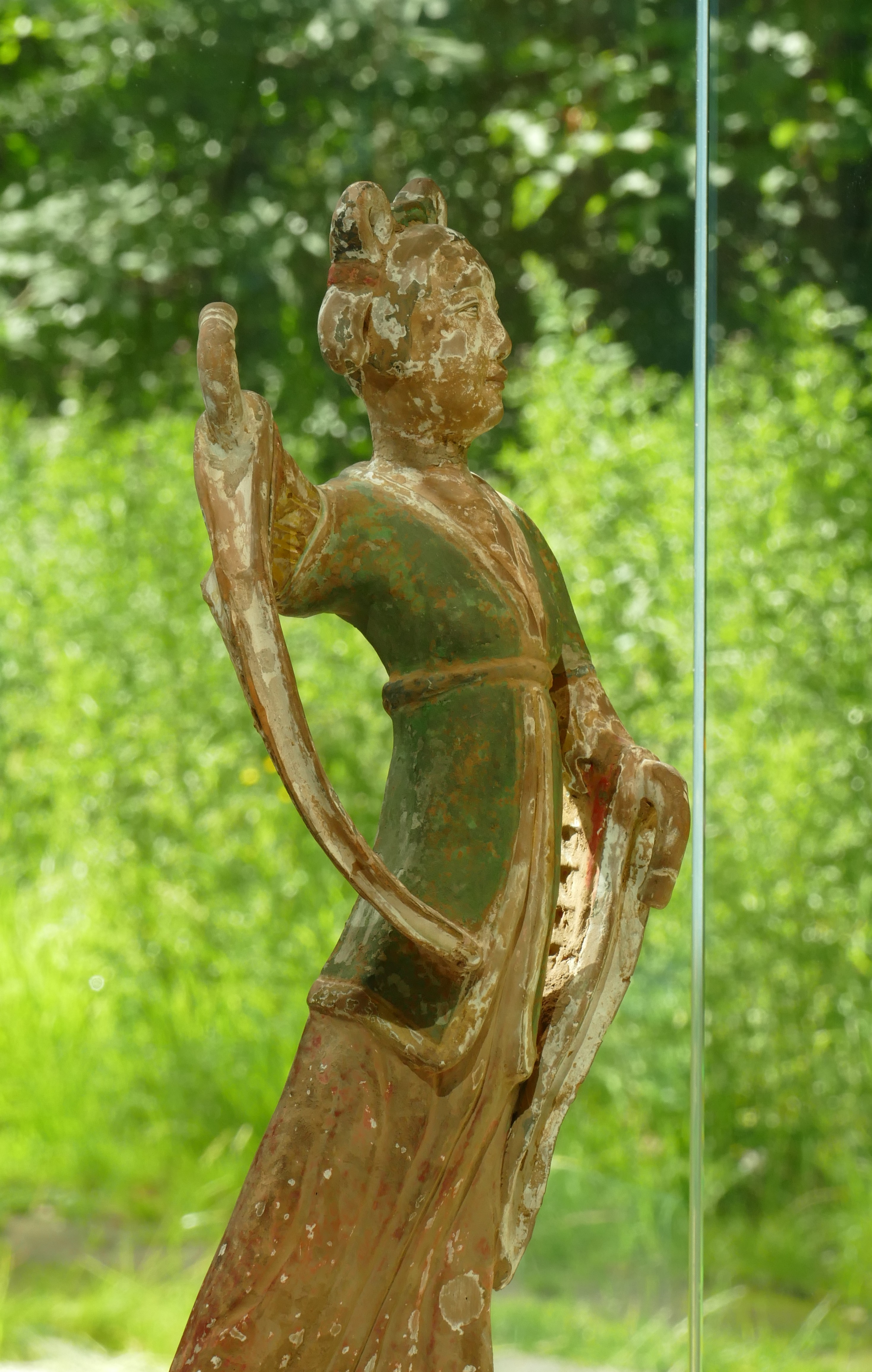 A statue of a dancer in an East Asian style. The dancer wears a green gown over a dress. The statue is somewhat worn.